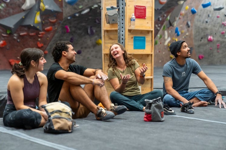 Four climbers sitting on the ground near a bouldering wall.