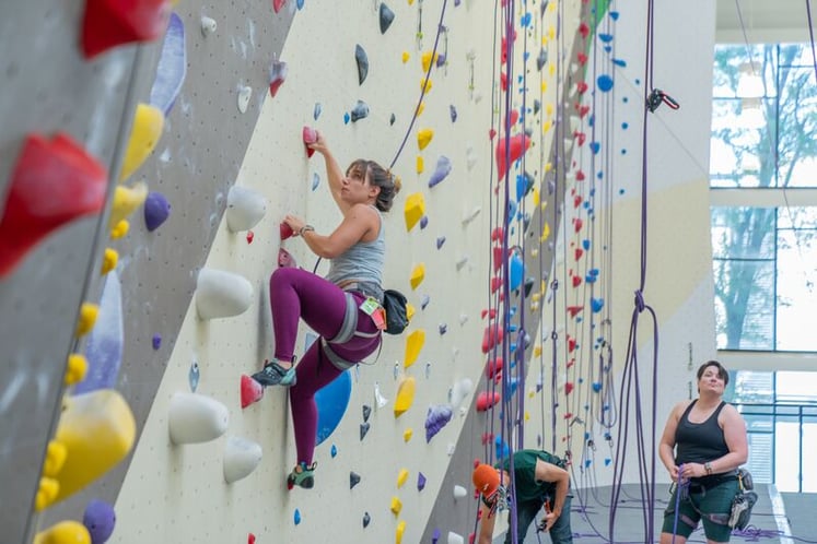 A beginner learning top-rope climbing with a belayer at a Movement gym