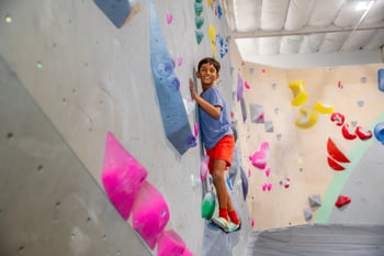 A kid smiling while bouldering at a Movement Gym